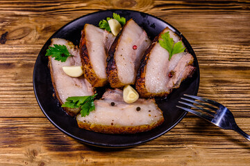 Slices of baked pork belly, garlic and parsley on a black plate