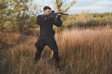 Young soldier in black uniform aiming an assault rifle.
