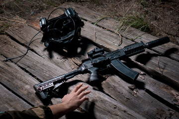 Hand reaching out an assault rifle and fbi helmet lying on a wooden surface.