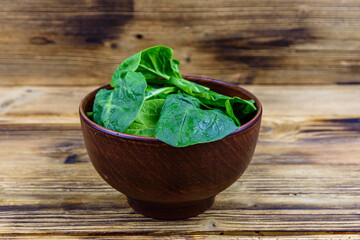 Ceramic bowl with spinach leaves on rustic wooden table