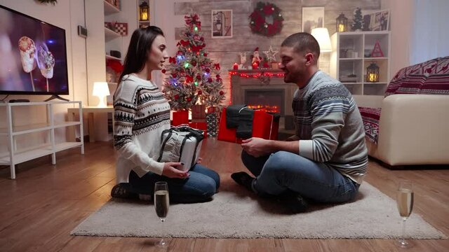 Zoom in shot of couple exchanging gifts on christmas day in front of fireplace. Champagne glasses .