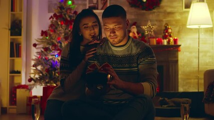 Beautiful young woman gives her handsome man a surprise gift on christmas day. Light comes out of the box. - Powered by Adobe