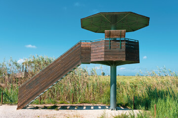 Bird watcher tower in Ebro Delta wetland area with rice field against a cloudy blue sky. Empty copy space for Editor's text
