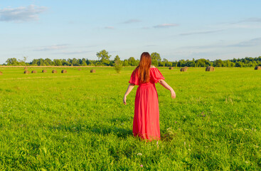 female model plus size in red dress on a field with haystacks, a beautiful young woman with brown hair, harvest concept