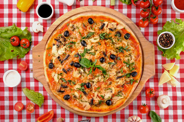 Rustic pizza with chicken meat, cheese, tomato, olive, mushrooms and tomatoes sauce, served on a wooden board for a dinner in italian restaurant background, top view. Classic Italy food. Close up