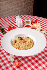 Flat lay. Creamy risotto with cherry tomatoes, rosemary and mushrooms in porcelain plate. Rustic style in italian restaurant background, top view. Italy food. Close up