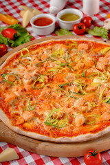 Rustic pizza macro with atlantic salmon, cheese, tomato, leek and tomatoes sauce on a wooden board for a dinner in italian restaurant background, top view. Classic Italy food. Pizza from wooden oven