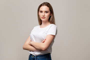 Confident woman. Female power. Portrait of successful lady in white t-shirt standing with crossed arms isolated on gray copy space background. Individuality determination.