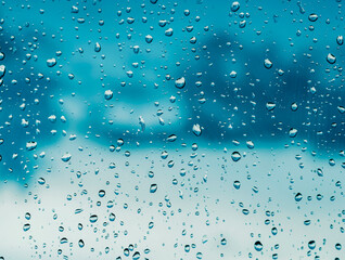 blue rain water drops on a window glass close up with deep dark storm clouds on thr backdrop,...