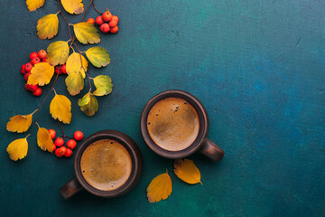 Obraz na płótnie Canvas Two brown clay cups of black coffee, branches with small autumn leaves and red Rowan's fruits on dark blue-green painted wooden background with empty space for text . Flat lay. Selective focus.