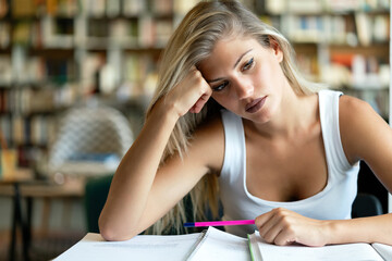 Portrait of a tired female student studying with books at the library