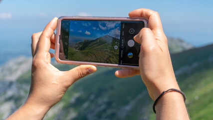 young woman holding a smartphone a taking a picutre of beautiful scenery of the Tatra mountains in Poland.
