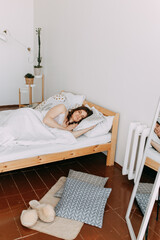 Cute beautiful brunette girl sleeping hugging a pillow lying in bed in a cozy bright bedroom at home, Scandinavian and modern  interior in the bedroom