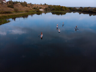 Fototapeta na wymiar Top view of tourists on lake with SUP-boards. Beautiful clear water with people floating on boards engaged in sup-surfing. Seascape with people rowing on boards on background horizon