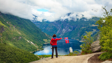 Fototapeta na wymiar Tourist over Geirangerfjord holds norwegian flag
