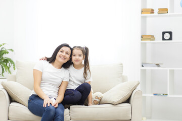 Photo of mother and her cute daughter posing on white sofa.