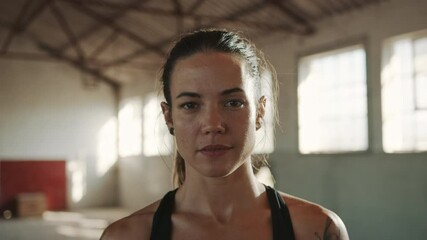 Portrait of a fitness woman inside abandoned warehouse after training session. Female athlete taking break from workout looking at camera.
