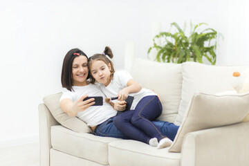 Happy mother and daughter sitting on the couch and taking selfie in the living room.