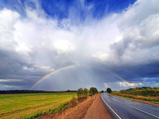 the phenomenon of a hemispherical rainbow in a natural landscape, fields, forests, road. the colorful spectacle of the appearance of a rainbow in late summer, autumn