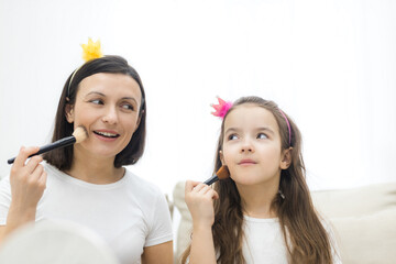 Photo of mother and her daughter holding cosmetics brushes over white background.
