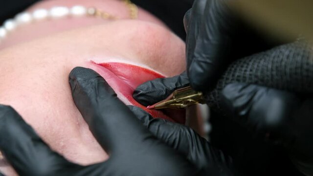 Cosmetologist making lips microblading permanent procedure using tattoo machine and pink pigment