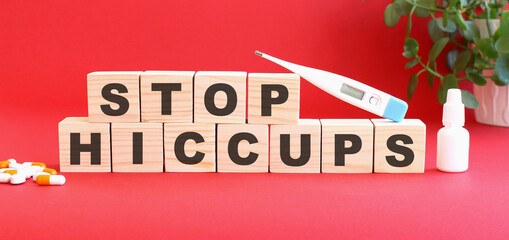 The words STOP HICCUPS is made of wooden cubes on a red background with medical drugs. Medical concept.