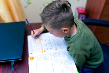 Close up side view of a schoolboy doing homework while sitting at a Desk at home. Reading books and completing lessons.