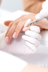 Obraz na płótnie Canvas Close up of manicurist using manicure scissors to remove cuticle of female nails in manicure salon