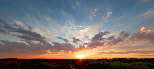 Panoramic view, beautiful sunset over the dunes, heavy clouds and sunset with sun rays, blue orange...