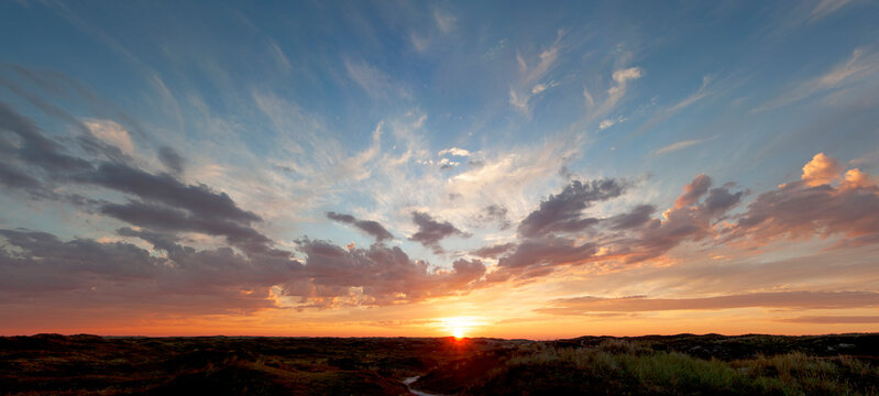 Panoramic view, beautiful sunset over the dunes, heavy clouds and sunset with sun rays, blue orange sky, sun in the middle, texel, Island