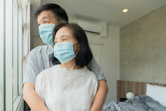 Portrait of Asian couple elder senior old male and female wearing face medical mask. pandemic coronavirus disease quarantine in home. Covid-19 outbreak prevention concept. - Powered by Adobe