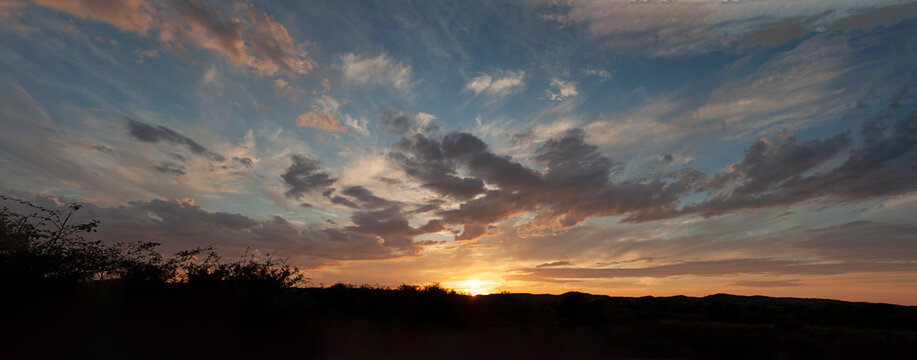 Sunset on dunes texel, panoramic view, clouds an sun going down, blue and orange, heavy clouds, 