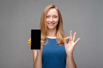 Portrait of beautiful smiling girl, holding mobile phone blank screen and showing OK gesture