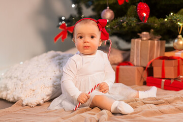 Obraz na płótnie Canvas holidays and childhood concept - sweet baby girl at christmas tree with gifts at home