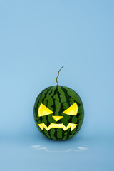 Glowing carved halloween watermelon on blue background. Green jack o lantern. Alternative Halloween pumpkin is a watermelon. 