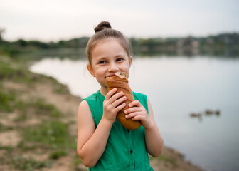 Little girl 5 years old in a beautiful green dress feeds the ducks with bread on the river bank