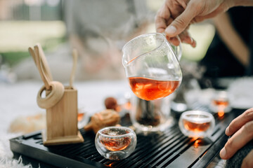 A male hand holds a glass teapot with freshly brewed red tea.