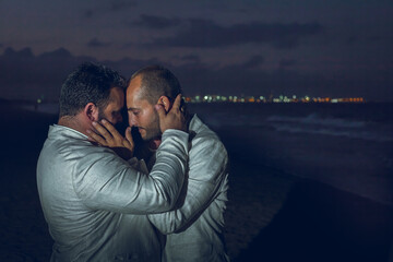 couple of two gay men hugging on the beach and wearing a groom suit at night