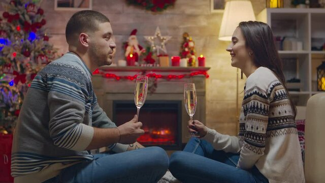 Couple having a conversation and drinking champagne while celebrating christmas in front of fireplace.