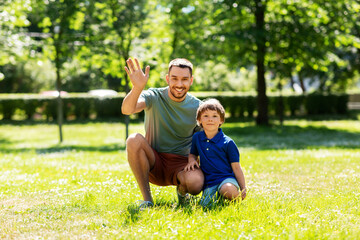 Fototapeta premium family, fatherhood and people concept - happy smiling father waving hand with little son at summer park