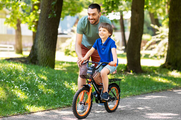 family, fatherhood and leisure concept - happy father teaching little son to ride bicycle at park