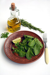 Vegetarian salad of spinach and basil with a slice of lime on a plate and a bottle of olive oil