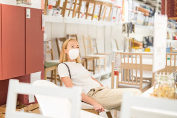 Fototapeta na wymiar New normal during covid epidemic. Caucasian woman shopping at retail furniture and home accessories store wearing protective medical face mask to prevent spreading of corona virus.