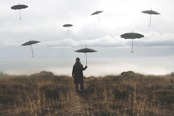 lonely man with umbrella walks down a road towards the lake and surreal black umbrellas fly in the...