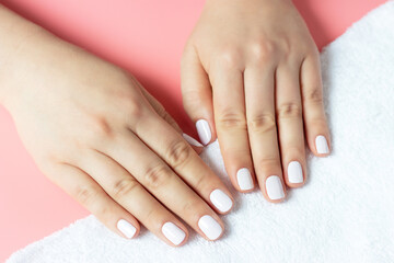 Beautiful women's hands with white manicure on pink and white background