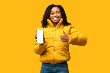 African Woman Showing Phone Blank Screen Gesturing Thumbs-Up, Yellow Background
