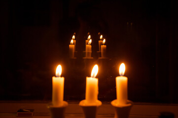 Three burning candles in multiple reflections. Flame of a candle on a dark background. Selective focus