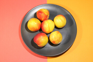 Group of colorful nectarine fruits or peach on a black plate. Colored background. Top view.