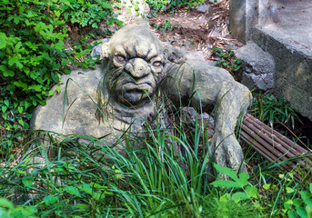 Fototapeta na wymiar Sculpture of a Troll sitting in a thicket near a stone bridge .