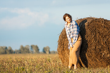 Pretty fresh  young woman  posing outdoors in field  and wearing in stylish clothes in the background a haystack, field  .Concept of summer  holidays at village  and live style